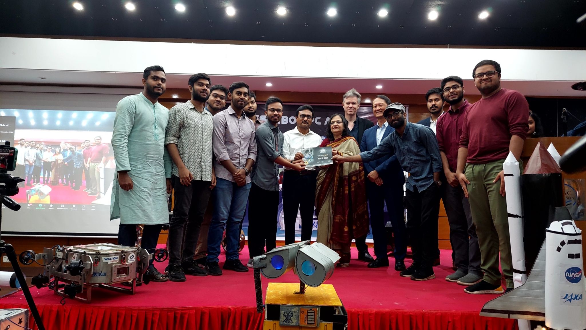 Teams and guests on stage at the Kibo Robot Programming Challenge award ceremony, with robot models in front